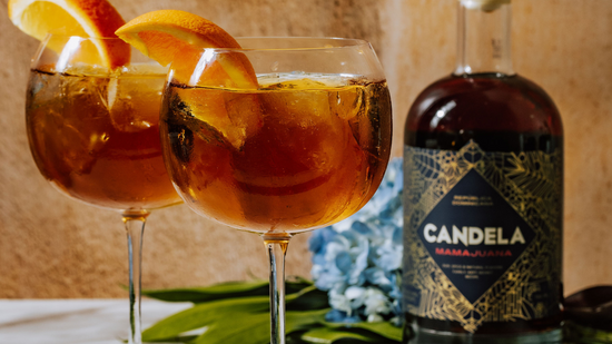 Candela Mamajuana's cocktail recipe, the Dominican Spritz, as a remix to the traditional Aperol Spritz. Image features two spiced rum spritz cocktails with seltzer water, served in a round wine glass over ice, and garnished with fresh orange slices.